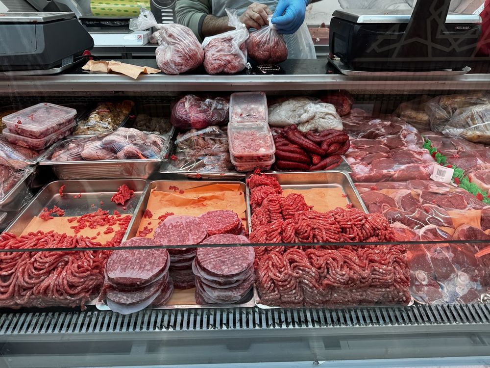 Close view along the counter, trays of mince, burgers, sliced cuts and sausages under glass